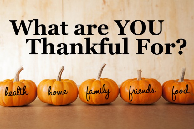 Five orange pumpkins sit in a row in front of a distressed, wooden background.