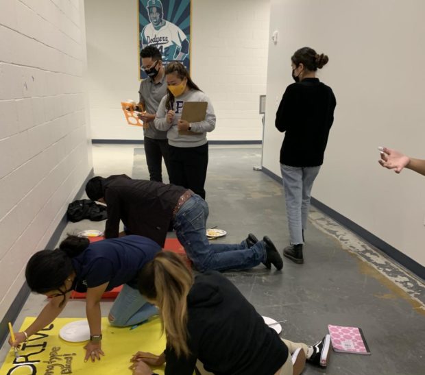 Students working on posters on the floor. Ms. Lee overseeing student work. 