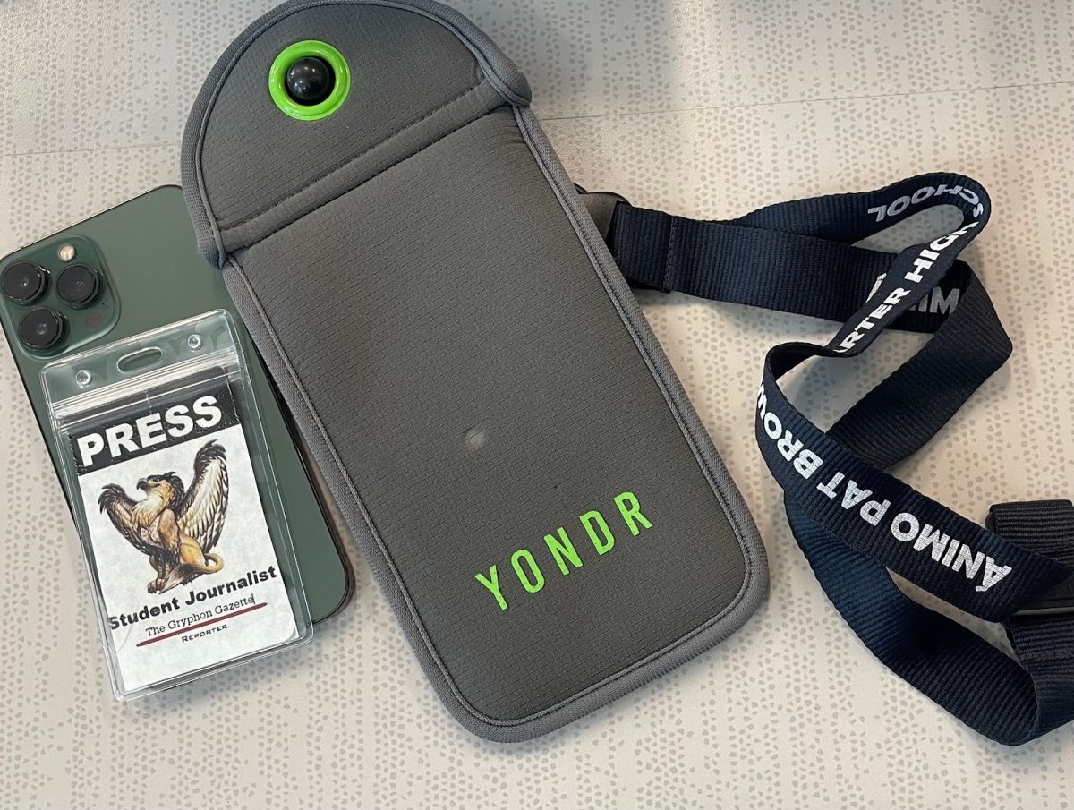 Yondr pouch on a student desk next to a student lanyard with a Gryphon Gazette Press Pass at the end of the lanyard.